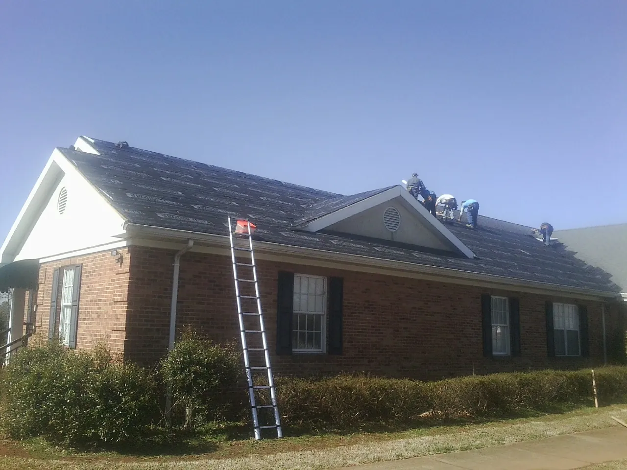 Crew tearing shingles off a brick ranch roof with a ladder set — Emergency Roof Repair work by our crew in Blair