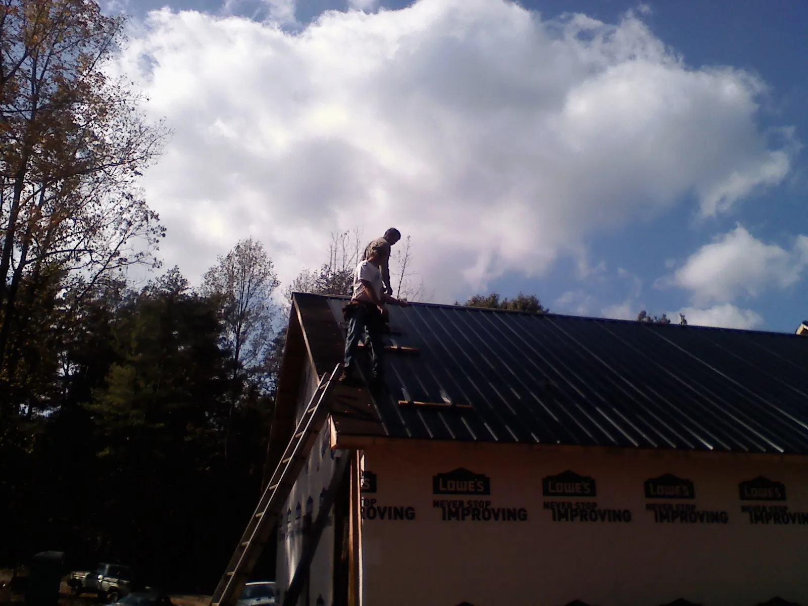 Roofer fastening dark metal panels high against a cloudy sky, from a Roof Inspection job in Blair