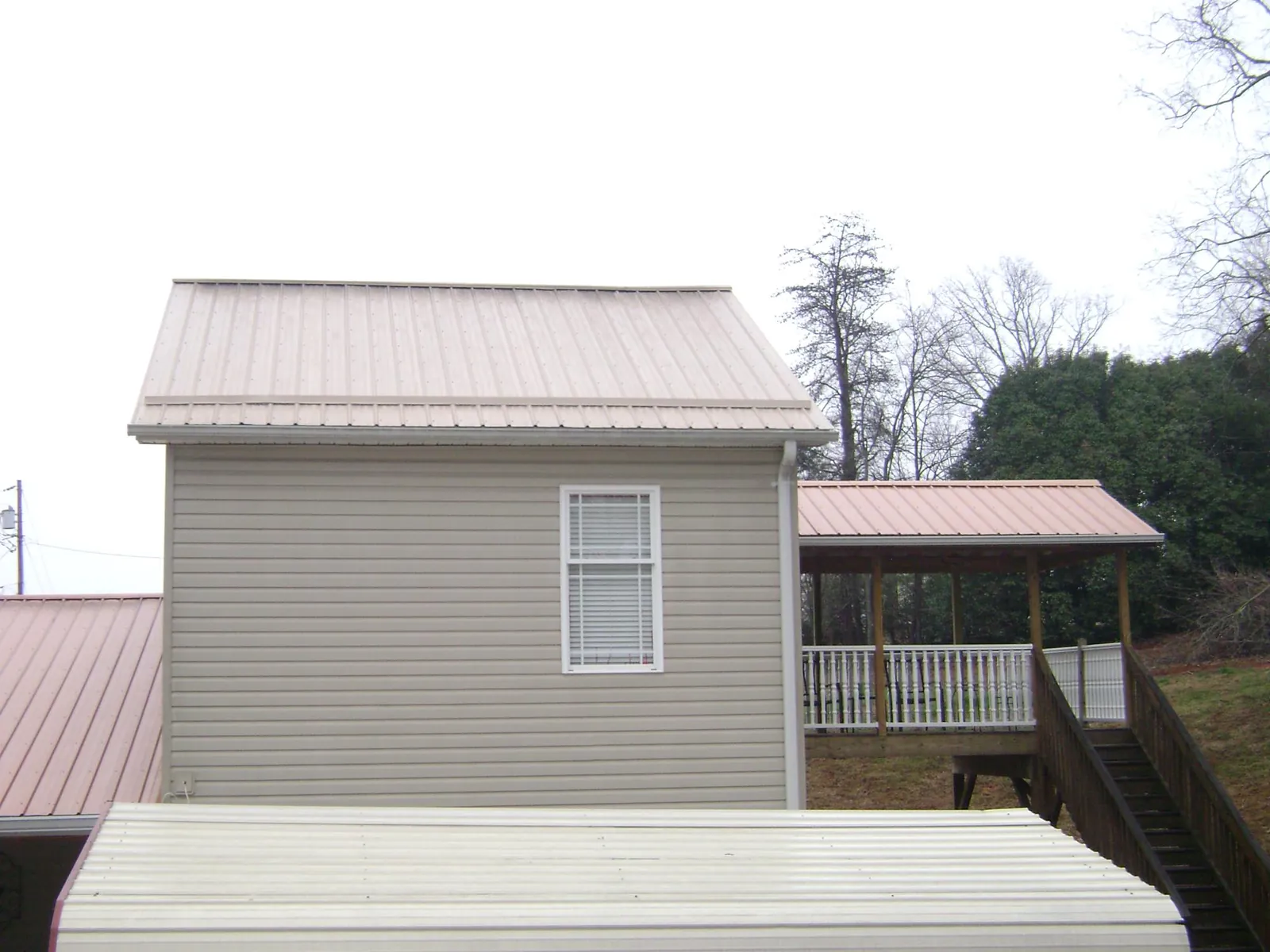 Tan metal roofs on a two story addition and attached porch, from a Roof Replacement job in Blair